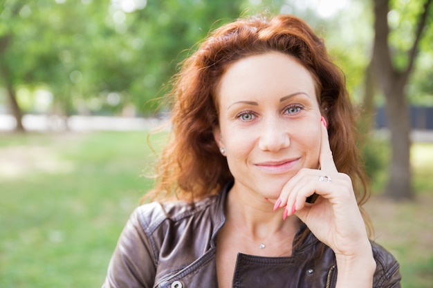 Smiling lady touching face and posing at camera in city park