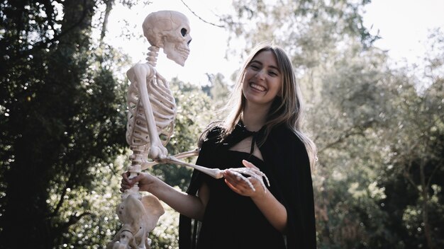 Smiling lady in witch clothes holding skeleton