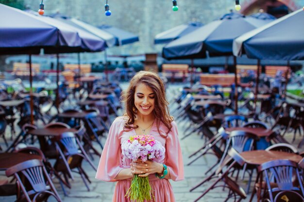 Smiling lady with flower bouquet stands among lonely tables in c