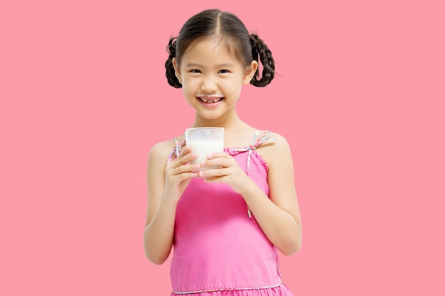 Smiling little Asian girl drinking milk isolated on pink background
