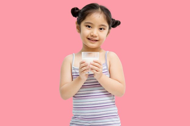 ピンクの背景に分離されたミルクを飲む小さなアジアの女の子の笑顔