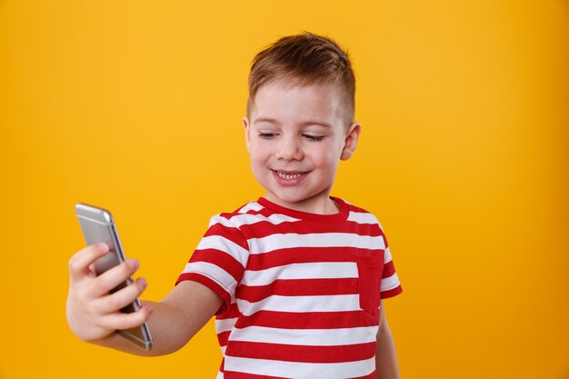 Smiling little boy holding mobile phone and making selfie