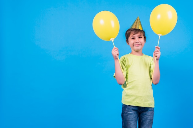 Улыбающийся мальчик держит желтые шары на синем фоне с копией пространства для текста