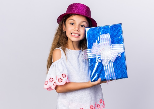 복사 공간 흰 벽에 고립 된 선물 상자를 들고 보라색 파티 모자와 함께 웃는 어린 백인 소녀