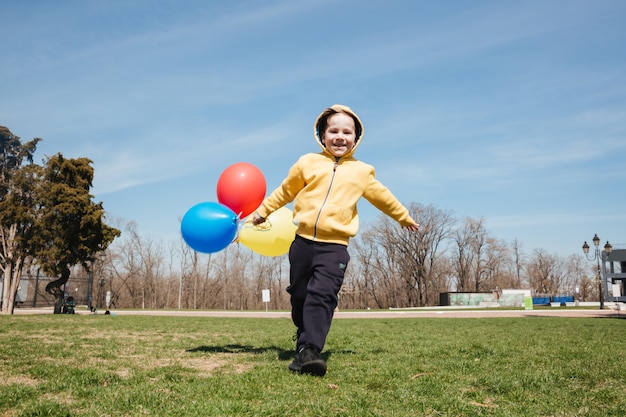 Smiling little children boy walking outdoors in park with balloons