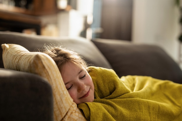 Smiling little girl covered with blanket sleeping on the sofa in the living room