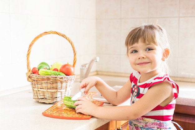 Free photo smiling little girl cutting cucumber with butter knife