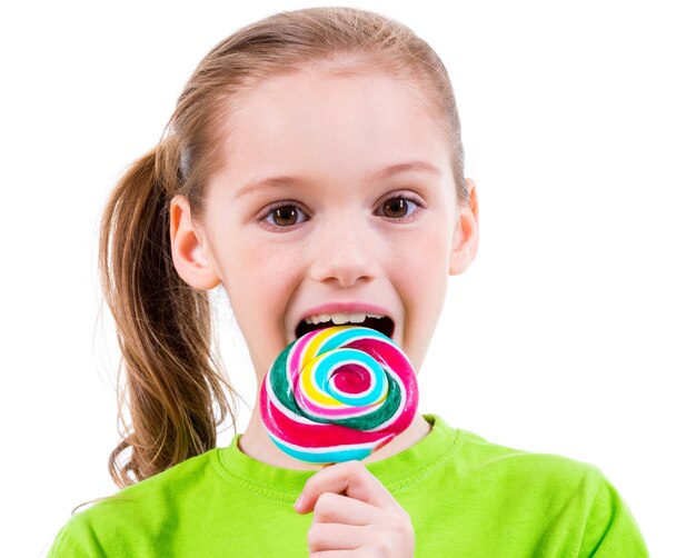 Smiling little girl in green t-shirt eating colored candy - isolated on white
