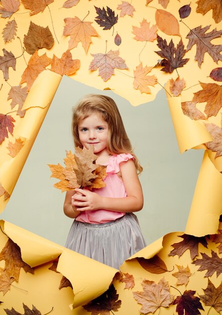 Smiling little girl playing with leaves and looking at camera. happy baby. cute little girl are preparing for autumn sunny day.