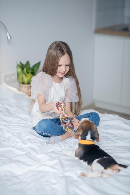 子犬にタグボートのおもちゃを見せてベッドに座っている小さな女の子の笑顔