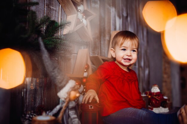 笑顔の小さな女の子が美しいクリスマスの装飾の間の棚に座って