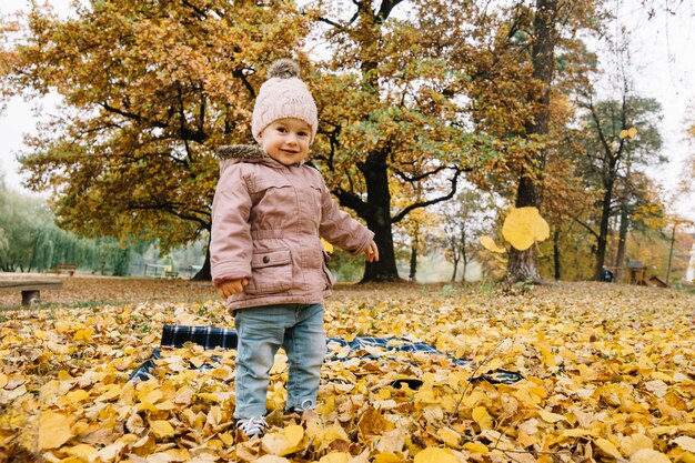 秋の森に立つ小さな女の子を笑顔