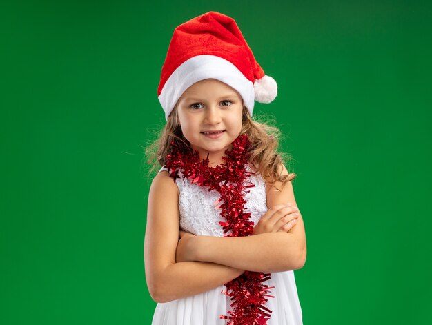 녹색 배경에 고립 손을 건너 목에 갈 랜드와 함께 크리스마스 모자를 쓰고 웃는 어린 소녀