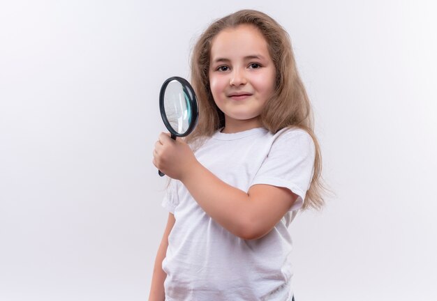 孤立した白い背景に拡大鏡を保持している白いTシャツを着て笑顔の小さな女子高生