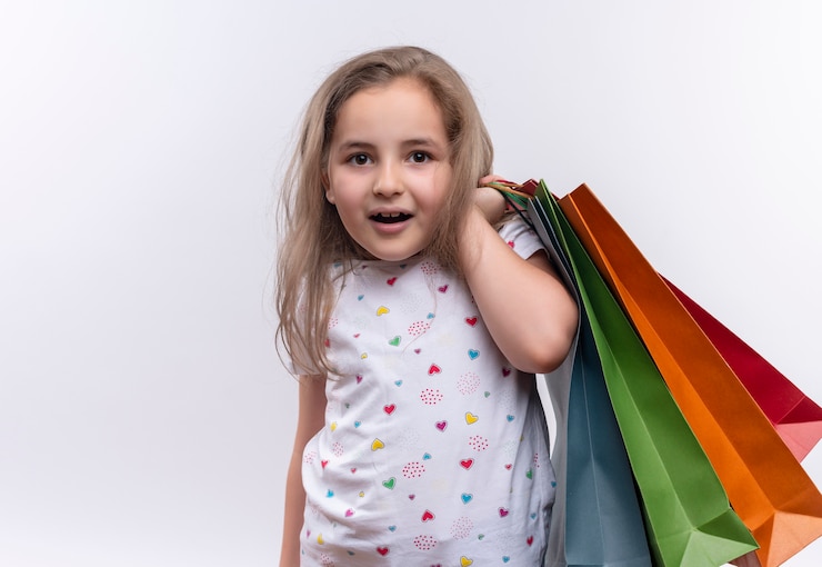 Free Photo smiling little school girl wearing white t-shirt holding paper bags on her shoulder on isolated white background
