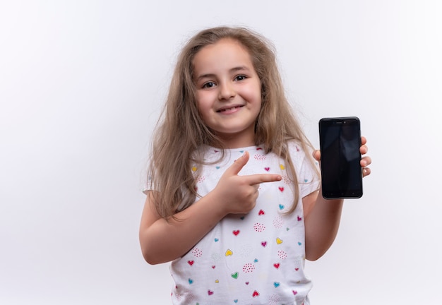 Free photo smiling little school girl wearing white t-shirt points to phone on isolated white background