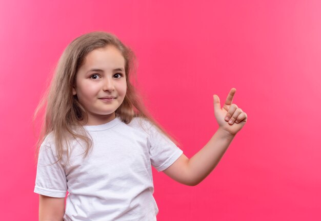 白いTシャツを着て笑顔の小さな女子高生は、孤立したピンクの背景に横を指しています