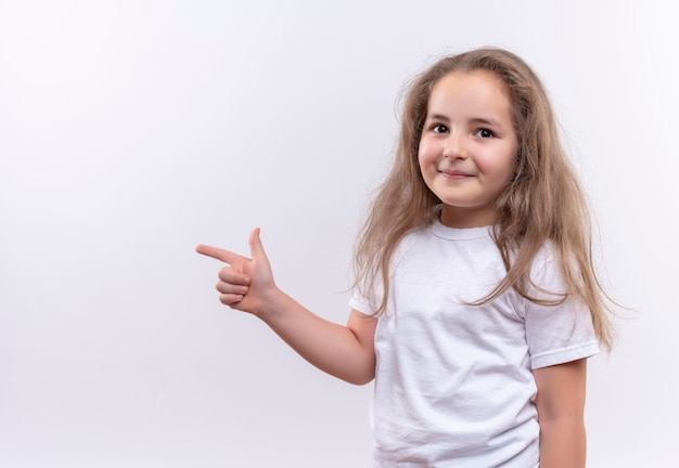 Smiling little school girl wearing white t-shirt points at side on isolated white background