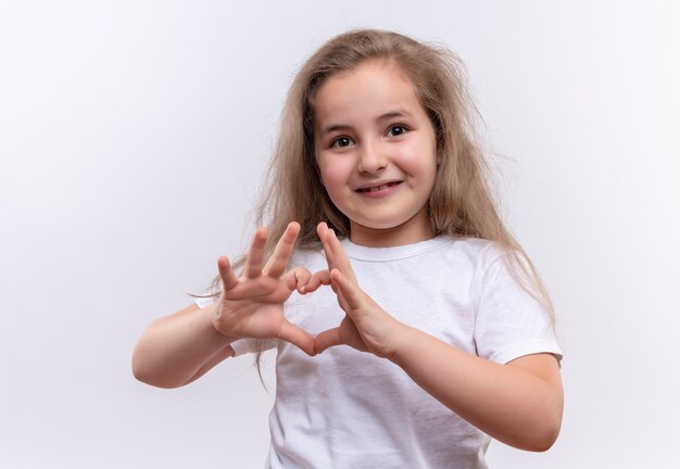 Улыбающаяся маленькая школьница в белой футболке показывает жест сердца на изолированном белом фоне