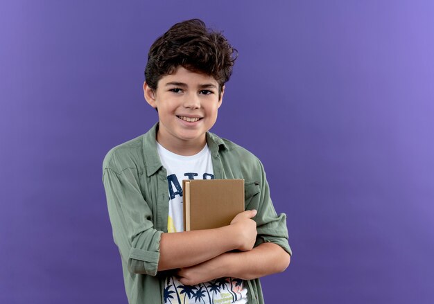 Smiling little schoolboy hugged books isolated on purple wall