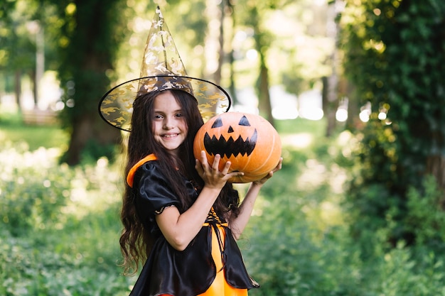 Smiling little witch holding pumpkin