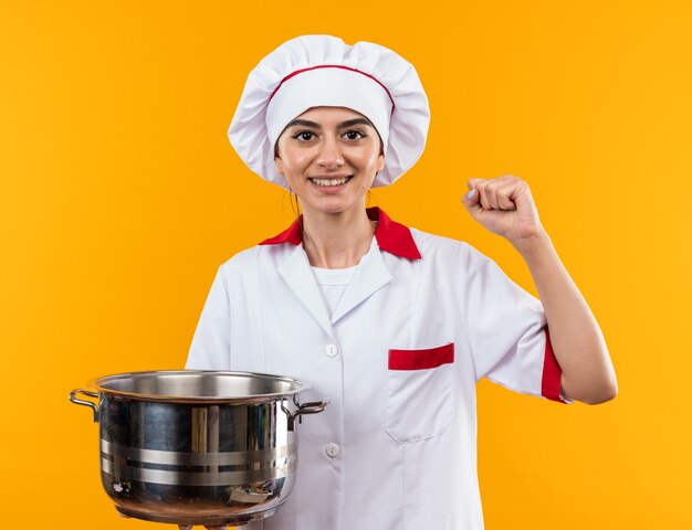 Smiling looking at camera young beautiful girl in chef uniform holding saucepan showing yes gesture 