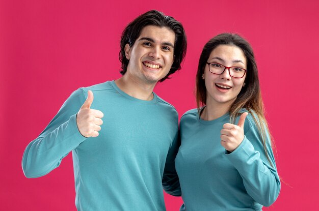 Smiling looking camera young couple on valentines day showing thumbs up isolated on pink background