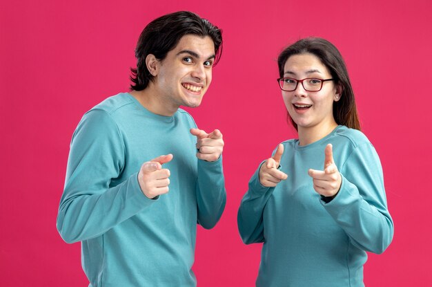 Smiling looking at camera young couple on valentines day showing you gesture isolated on pink background