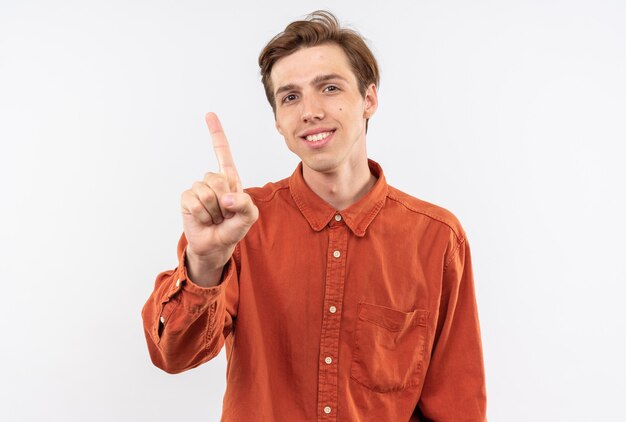 Smiling looking camera young handsome guy wearing red shirt showing one isolated on white wall