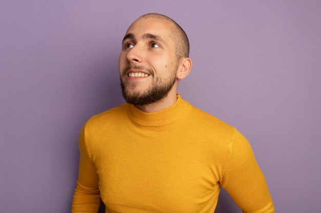 Smiling looking at side young handsome guy isolated on purple wall