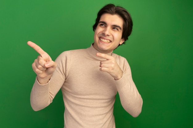 Smiling looking at side young handsome guy points at side isolated on green wall with copy space