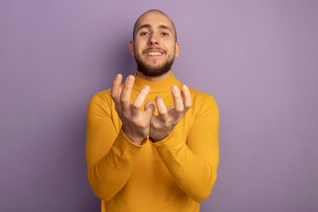 コピースペースと紫に分離された手を一緒に持っている若いハンサムな男をまっすぐに見ている笑顔