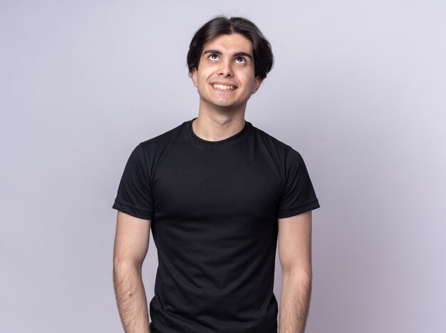 Smiling looking up young handsome guy wearing black t-shirt isolated on white wall with copy space