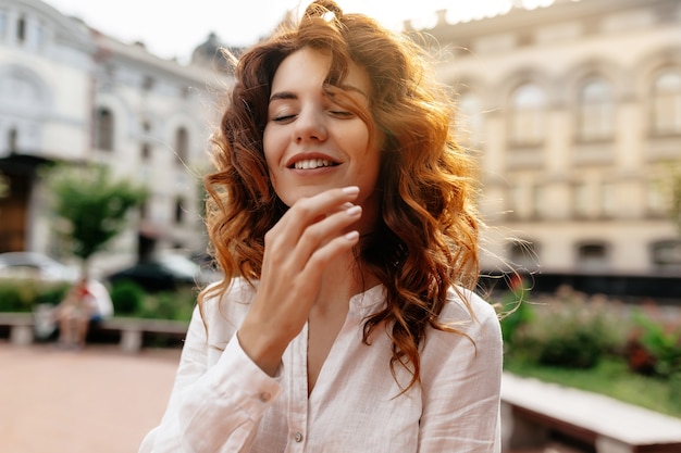 Smiling lovable charming lady with curly red hair smiling with closed eyes in sunlight