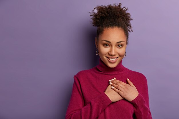 Smiling lovely curly woman impressed by touching moment, presses palms to chest