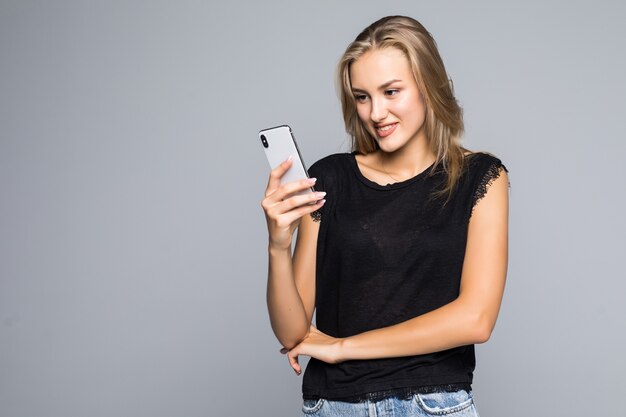 Smiling lovely young woman standing and using cell phone over grey background