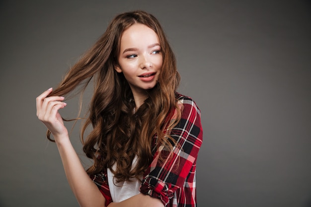 Smiling lovely young woman touching her hair and looking away