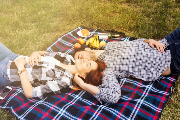 Smiling loving young couple lying on blanket over the green grass