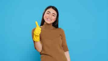 Free photo smiling maid wearing yellow rubber gloves while doing ok gesture after finishing to clean client house, posing in studio. cheerful housekeeper is responsible for providing cleaning services