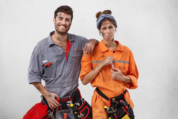 Smiling male carpenter tries to encourage his female colleague who has upset and tired expression