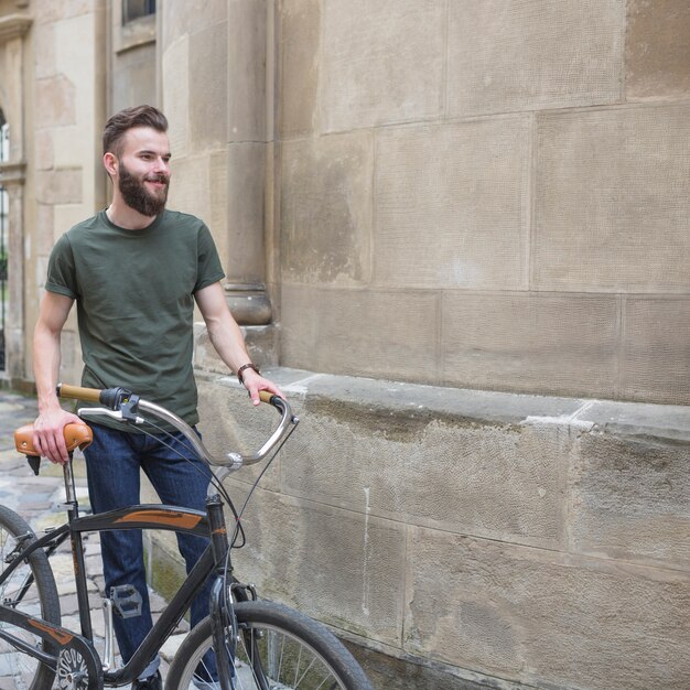 Smiling male cyclist with his bicycle standing beside stone wall