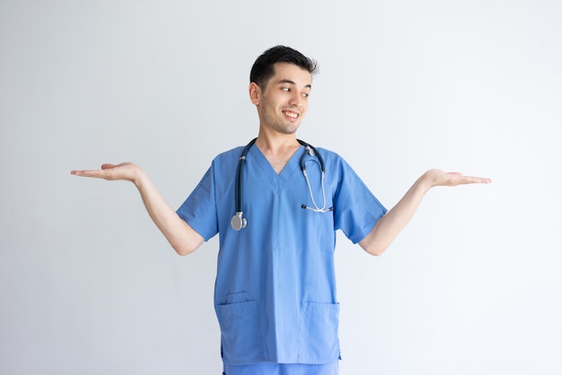 Free photo smiling male doctor holding empty space with both hands