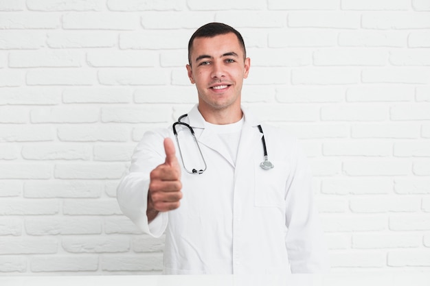 Smiling male doctor posing in front of white bricks wall