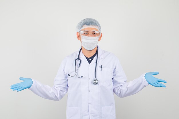 Smiling male doctor in protective clothes shrugging lifting shoulders and looking confused