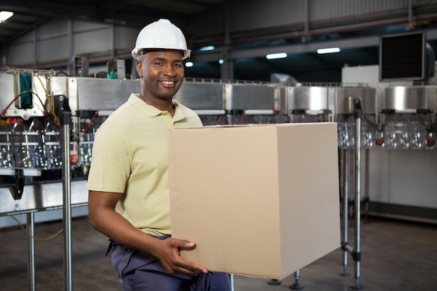 Улыбающийся сотрудник-мужчина, несущий картонную коробку на фабрике соков