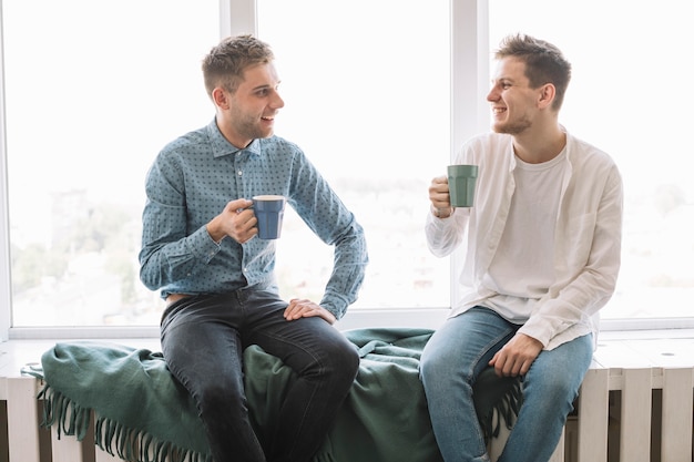 Smiling male friends sitting near window having drinking coffee