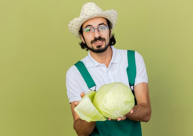 Smiling male gardener in optical glasses wearing gardening hat holds cabbage