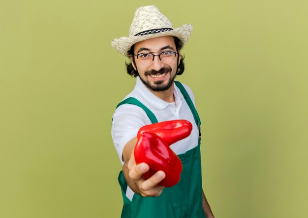 Smiling male gardener in optical glasses wearing gardening hat holds red peppers 