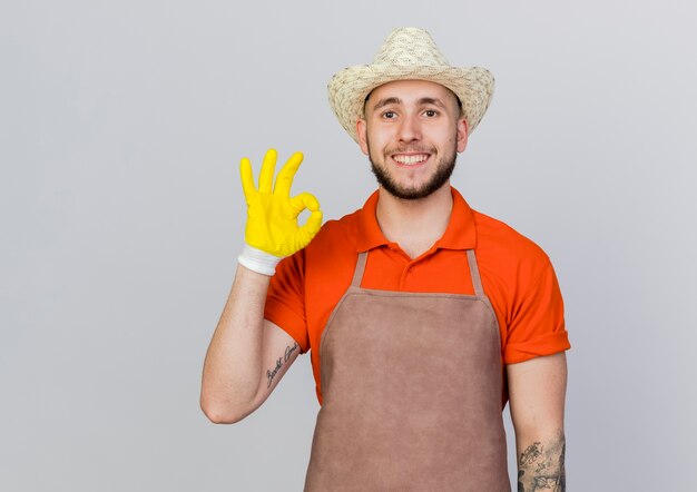 Smiling male gardener wearing gardening hat and gloves gestures ok hand sign 