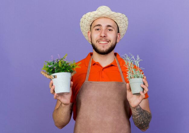 Smiling male gardener wearing gardening hat holds flowerpots